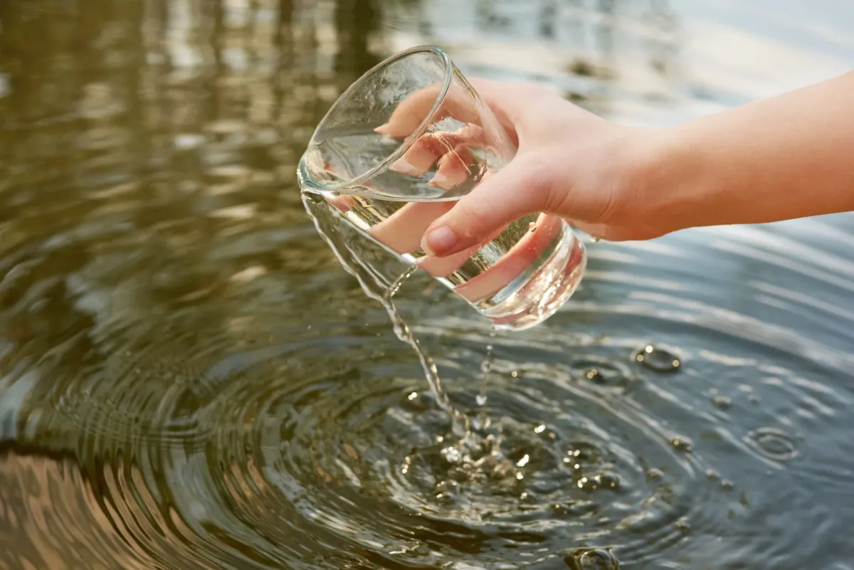 A hand holding a glass over water