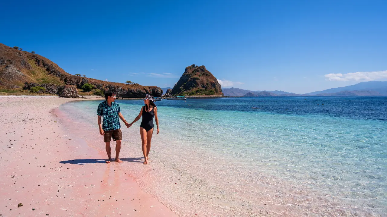 A couple holding hands walking along Pink Beach (Pantai Merah) in Komodo, Indonesia