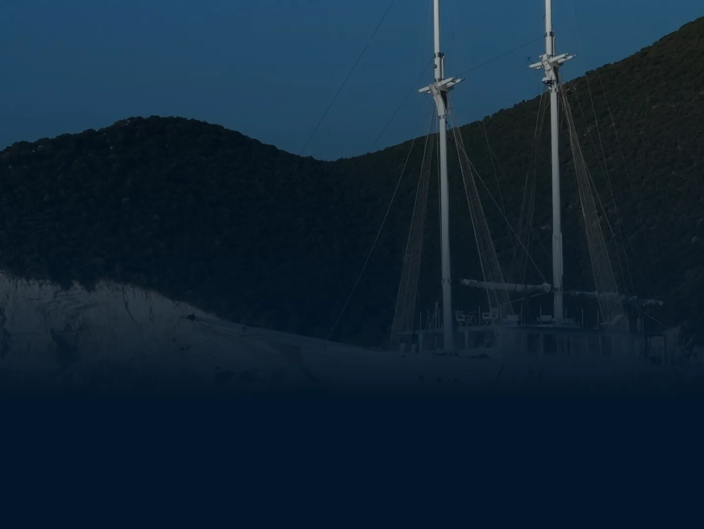 Sailing yacht moored beside forested hillside at dusk